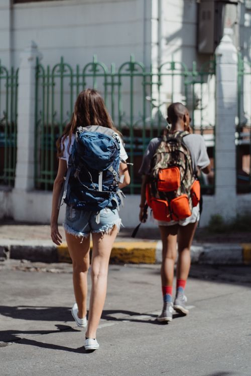 Free Two young adults walking with backpacks in a vibrant urban setting. Stock Photo