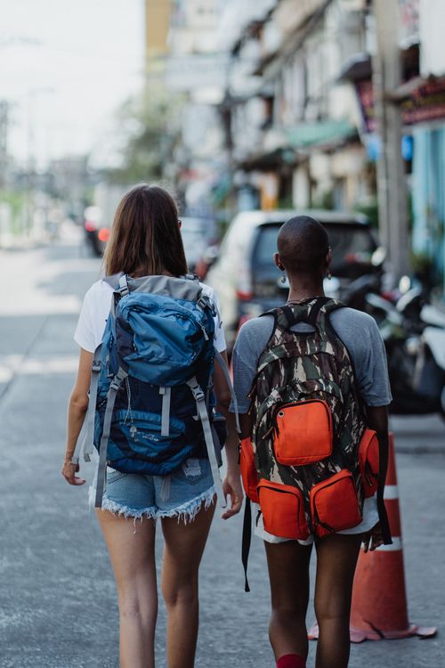 Free Two women with backpacks walk through an urban street, capturing the spirit of adventure and exploration. Stock Photo
