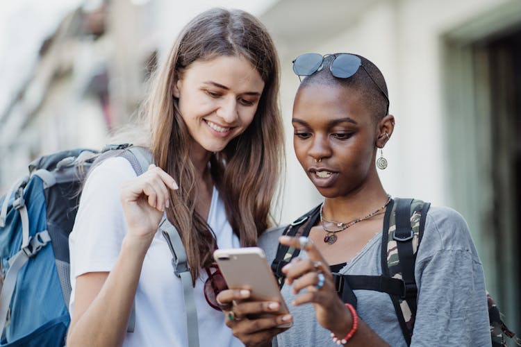 Women Travelers Visiting City With Backpacks Using Smart Phone