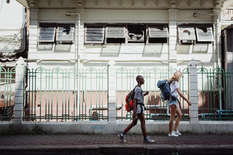 Two women walking with backpacks on a city sidewalk, embracing urban exploration.