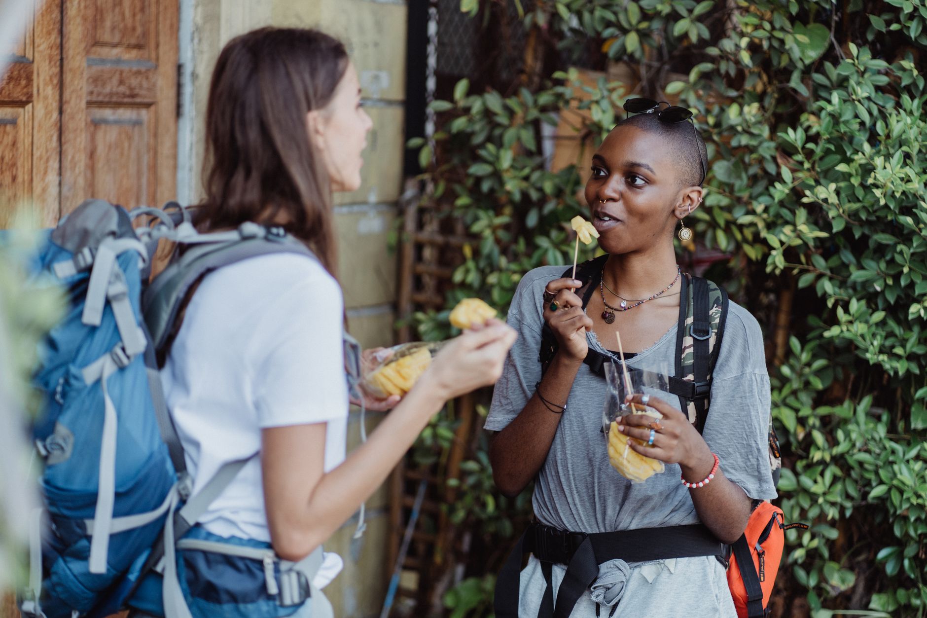 Two women hikers enjoying fresh fruit while backpacking outdoors, capturing a vibrant lifestyle moment.