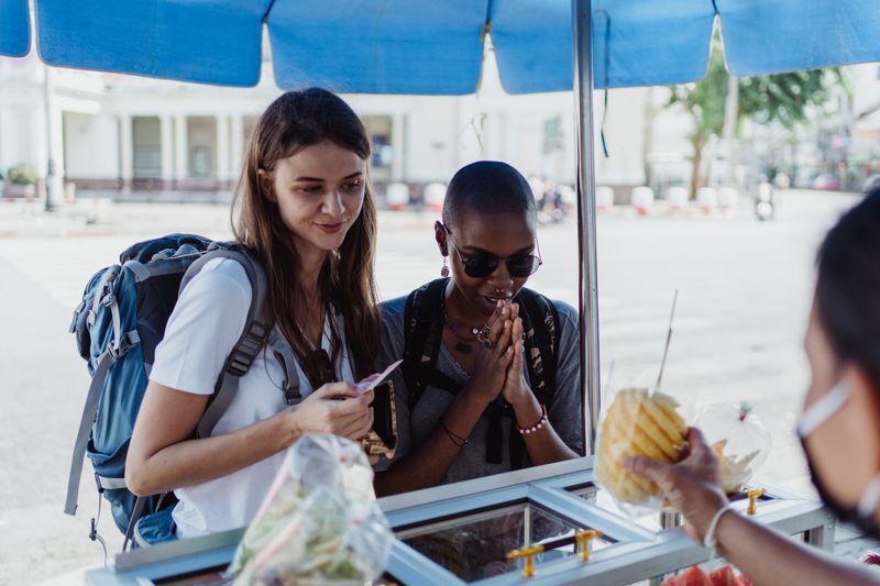 Two travelers buying fruit from a street cart — Ketut Subiyanto on Pexels