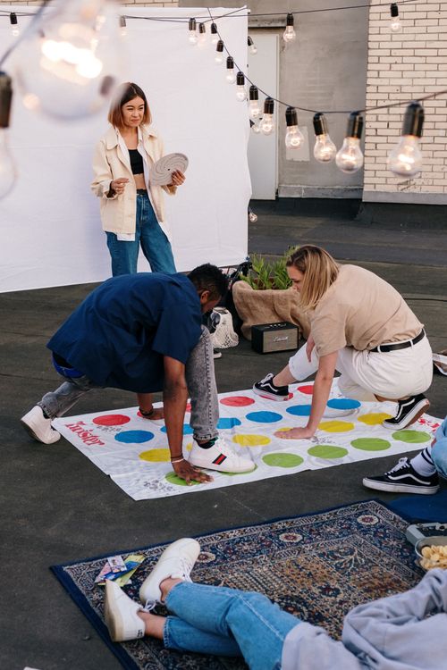 Free A group of friends playing Twister on a cozy rooftop setting with string lights. Stock Photo