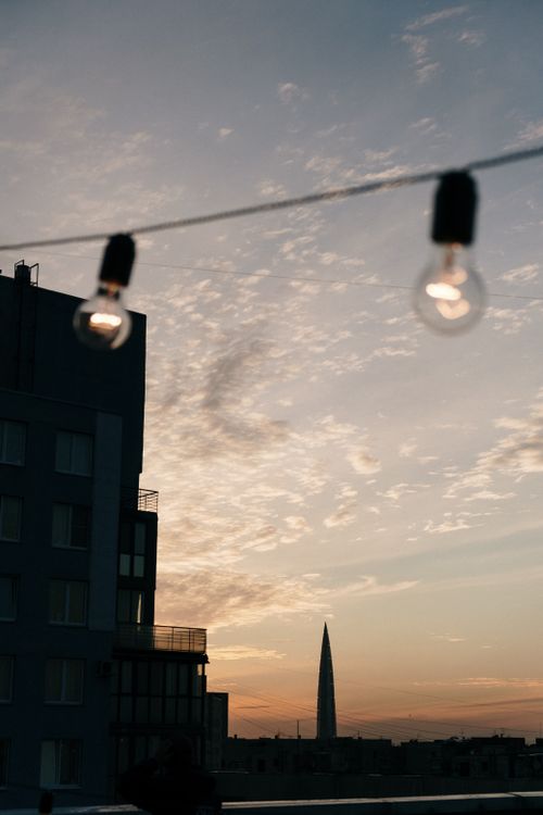 Free Urban sunset view with city skyline and illuminated rooftop string lights. Stock Photo