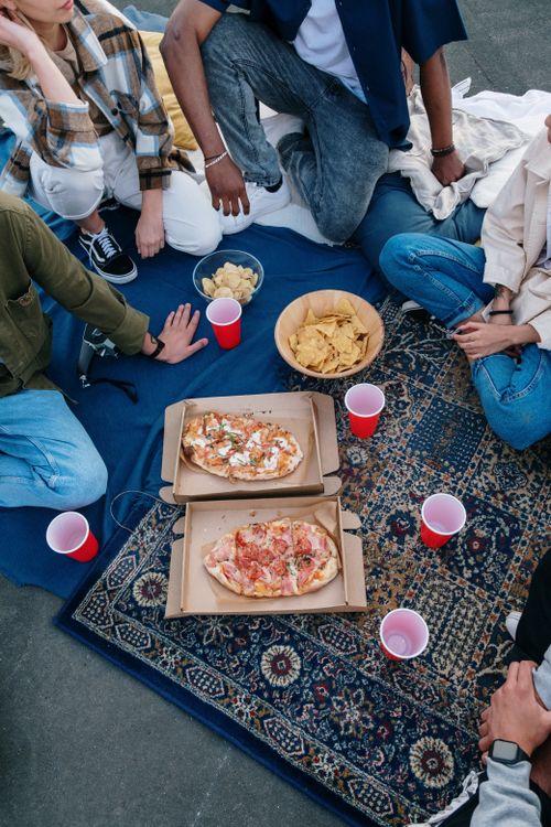 Free A group of friends enjoying pizza on a rooftop picnic with red cups and chips. Stock Photo