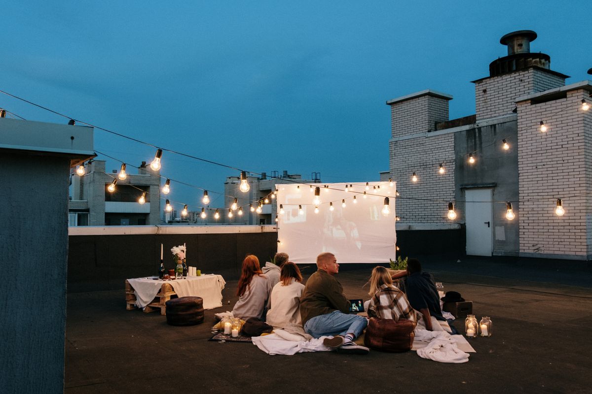 Friends sitting together under string lights at an open-air film screening — photo by cottonbro studio on Pexels