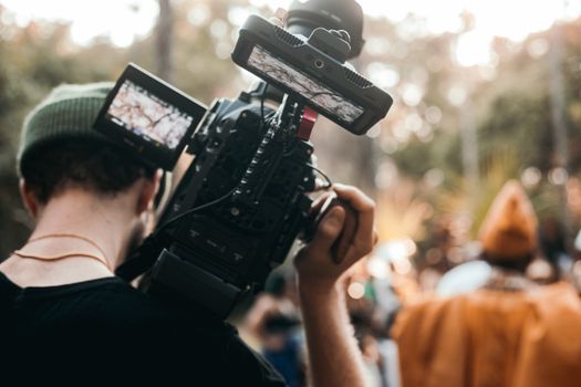 Man with a beanie filming an outdoor scene using professional camera equipment.