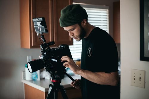 Free A bearded man with a beanie operates camera equipment indoors, focusing intently. Stock Photo