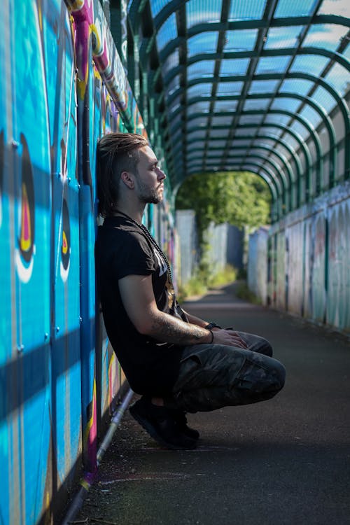 Stylish man sitting near wall with graffiti