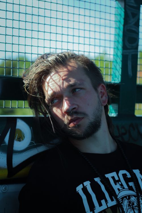 Free Stylish brown haired male with beard and piercing leaning on metal fence with graffiti and looking away Stock Photo