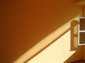 温暖的阳光透过敞开的窗户，在黄色墙壁上投下鲜明的阴影，构成了一幅极简主义的画面