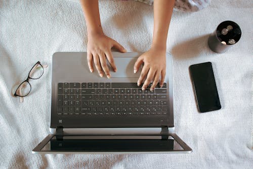 Free Crop freelancer typing on laptop near smartphone on bed Stock Photo