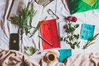 From above of colorful calendar near plant sprigs and mug of hot drink on creased fabric with perfume and smartphone