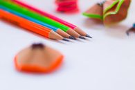 From above closeup of bright multicolored pencils with pointed leads near dry shavings on white desk