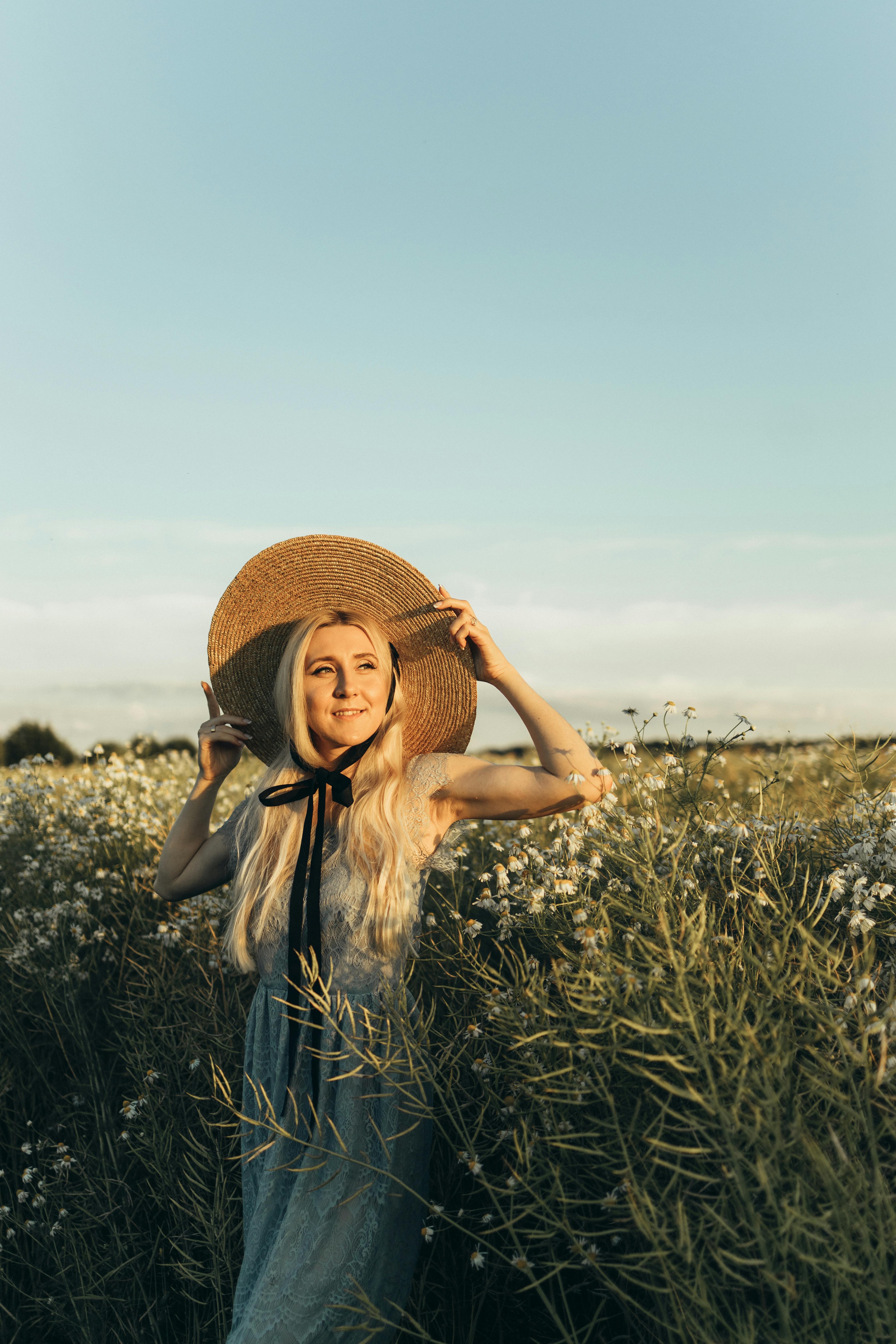 花田里的女人戴着草帽，穿着白色连衣裙，在阳光明媚的天空下微笑