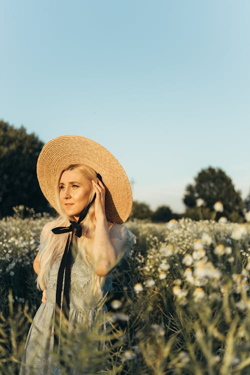 Woman in a Dress and Sun Hat Standing on Flower Field