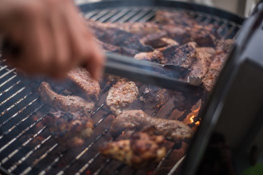 Close-up of sizzling meat on an outdoor grill with a hand using tongs. Perfect for summer barbecue themes.