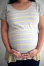 Crop faceless pregnant woman touching belly with both hands