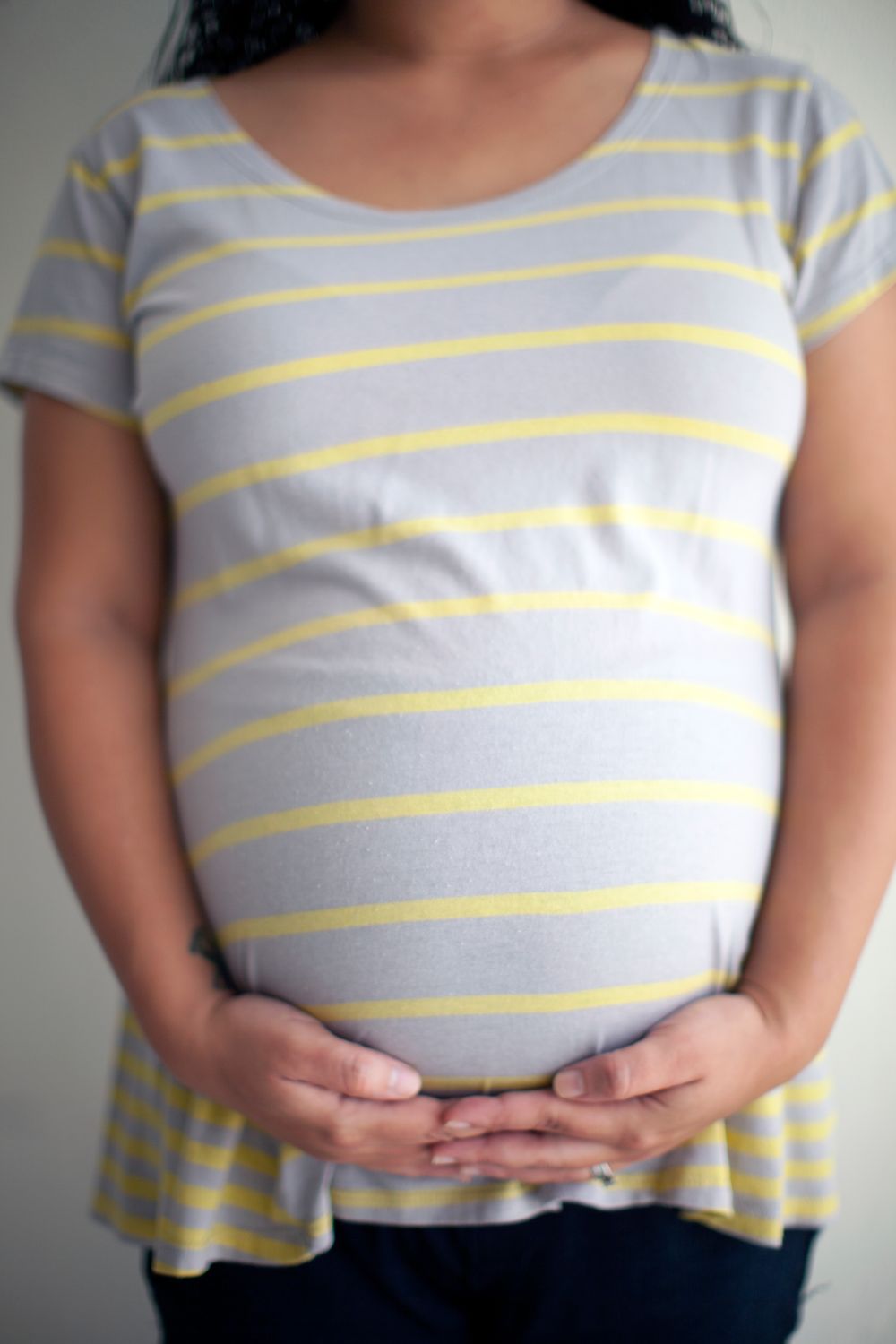 Hands gently holding a pregnant belly covered by a striped shirt