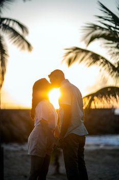 Side view silhouettes of loving couple holding hands and kissing while spending picturesque sunset on exotic beach