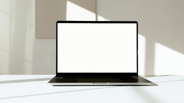 A laptop with a blank white screen on a desk, bathed in natural sunlight.