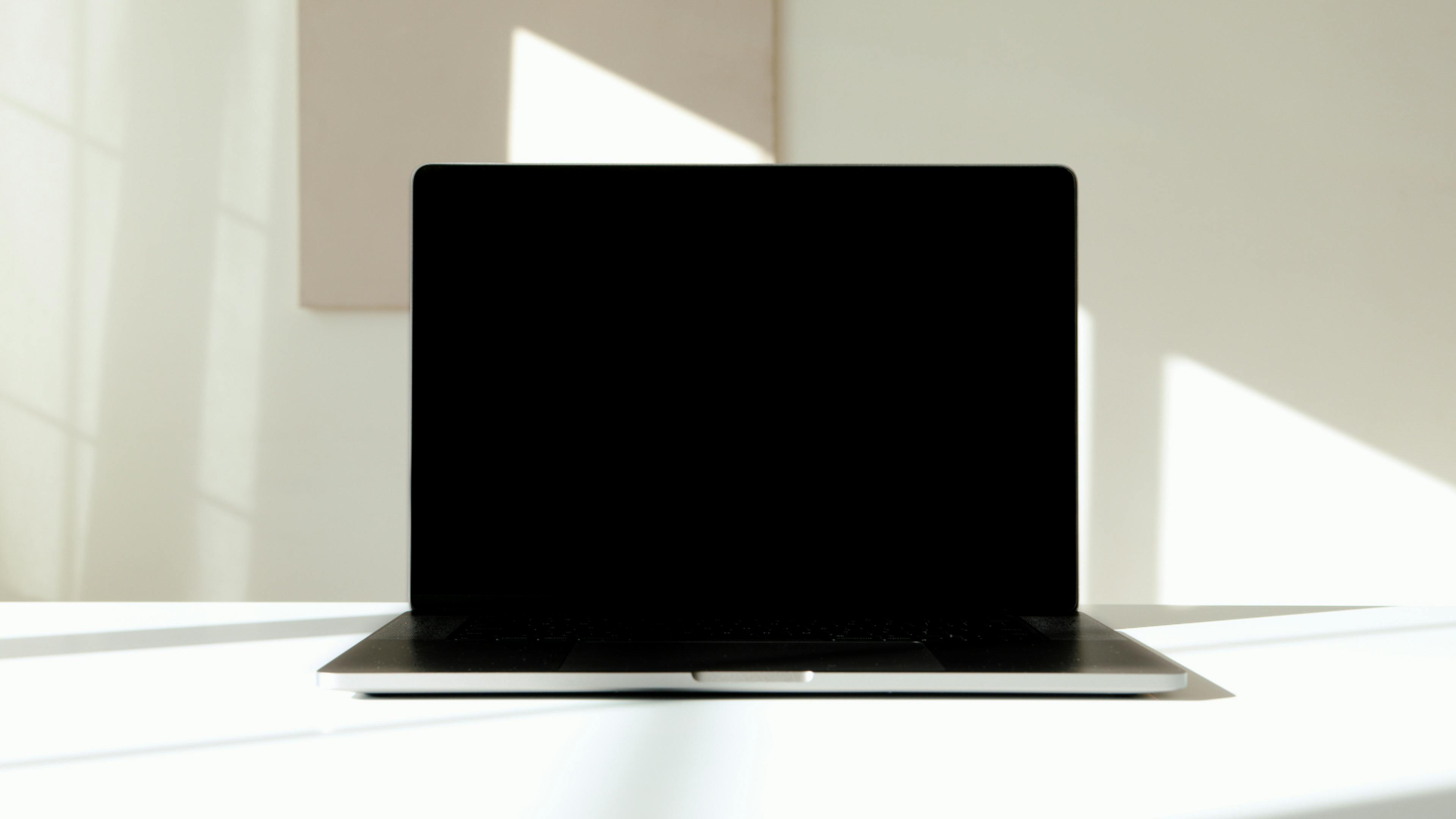 A modern laptop with a black screen on a sunlit white surface, highlighting sleek design.