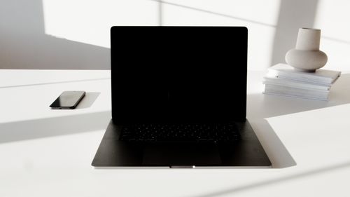 Free A minimalist white desk featuring a laptop, smartphone, and decorative vase in a modern setting. Stock Photo