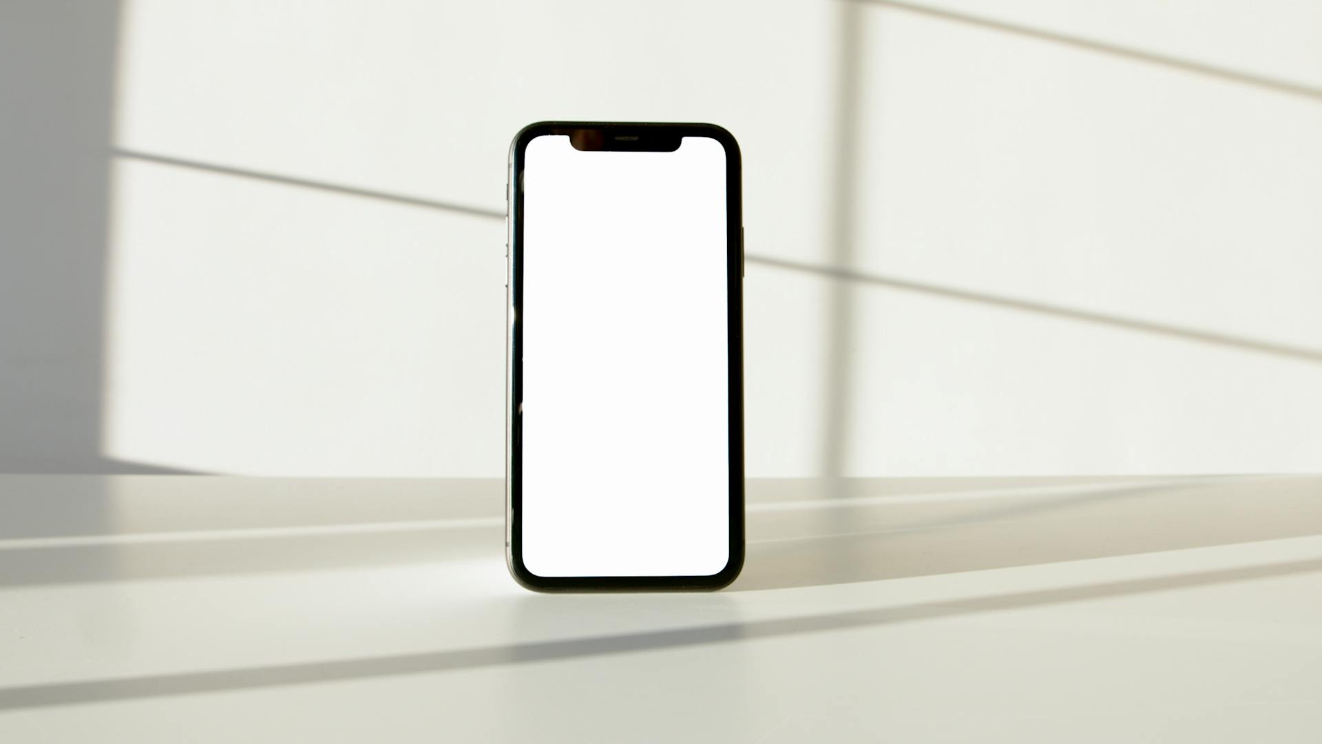 Modern smartphone with a blank screen placed on a minimalist white surface, ideal for design mockups.