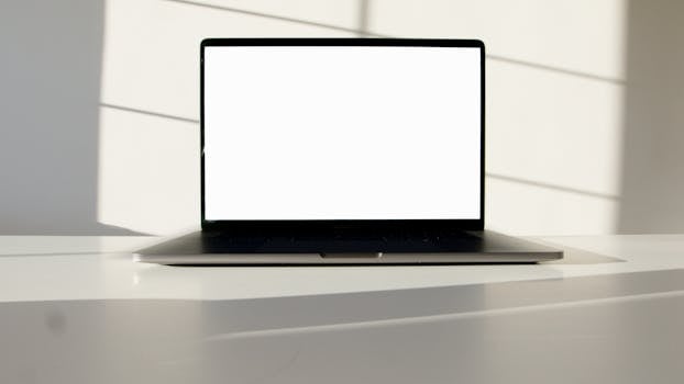Laptop with blank screen on a white table in sunlit room, perfect for mockup presentations.