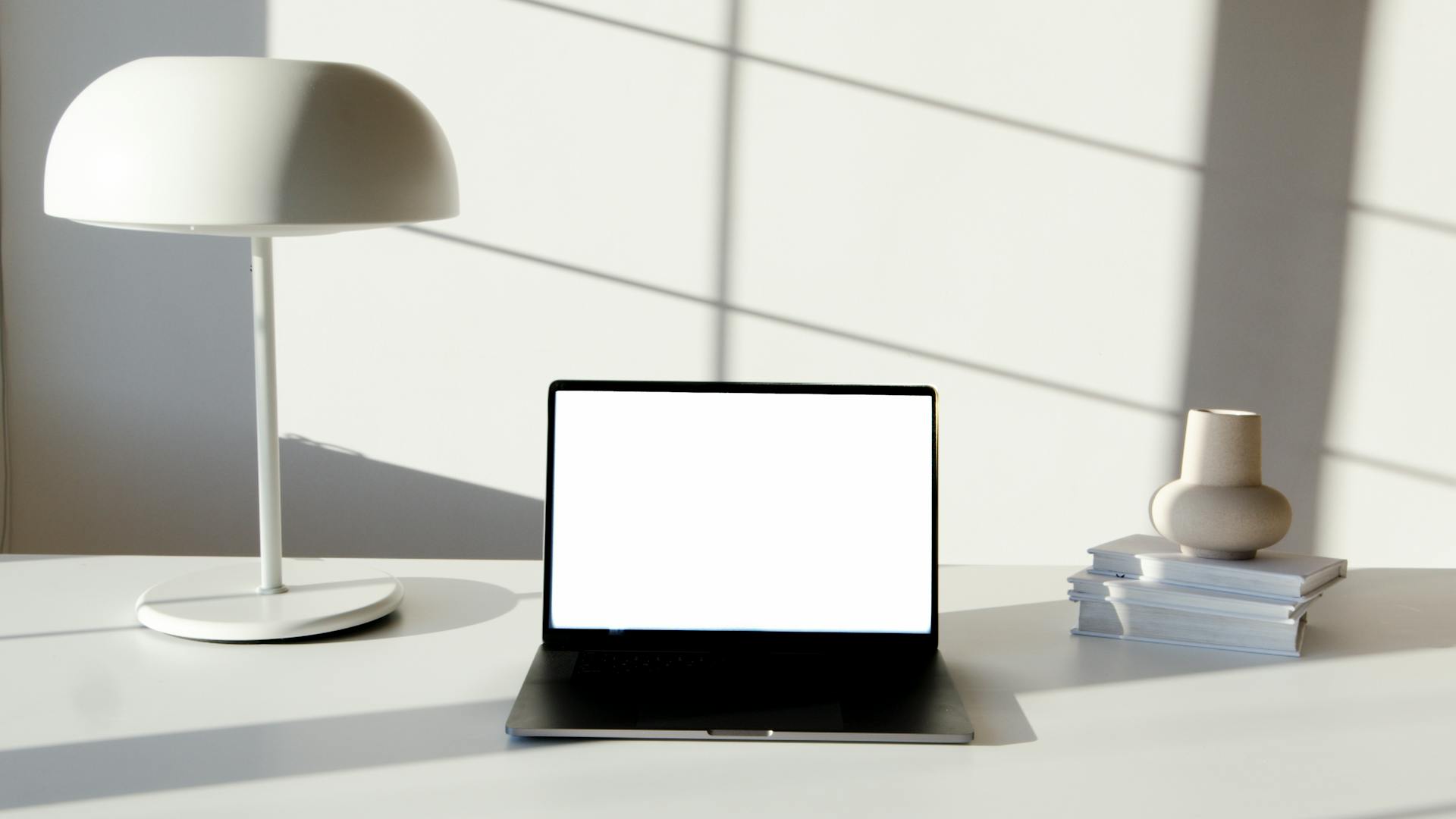 Sleek office desk setup featuring laptop, modern lamp, and decorative vase in soft lighting.