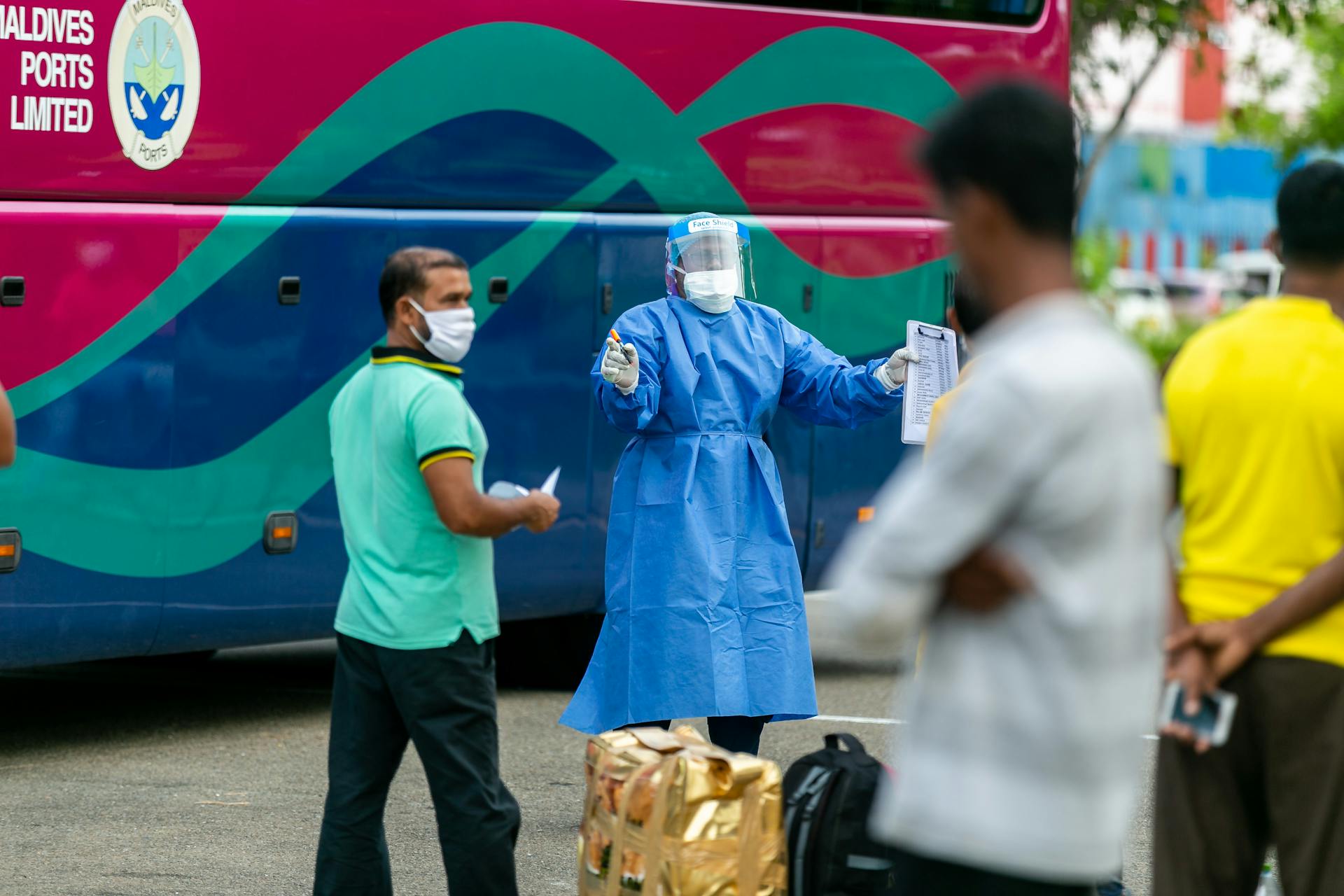 Healthcare worker in PPE directing people during pandemic, emphasizing safety and travel protocols.