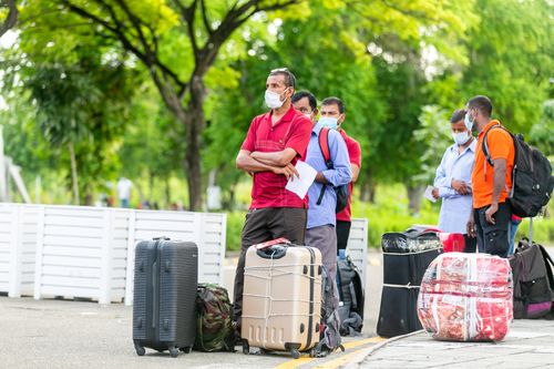 Free People standing with suitcases wearing masks outdoors, indicative of travel during COVID-19 times. Stock Photo
