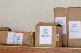 Blue emblem sticker of World Health Organization on carton boxes heaped on table
