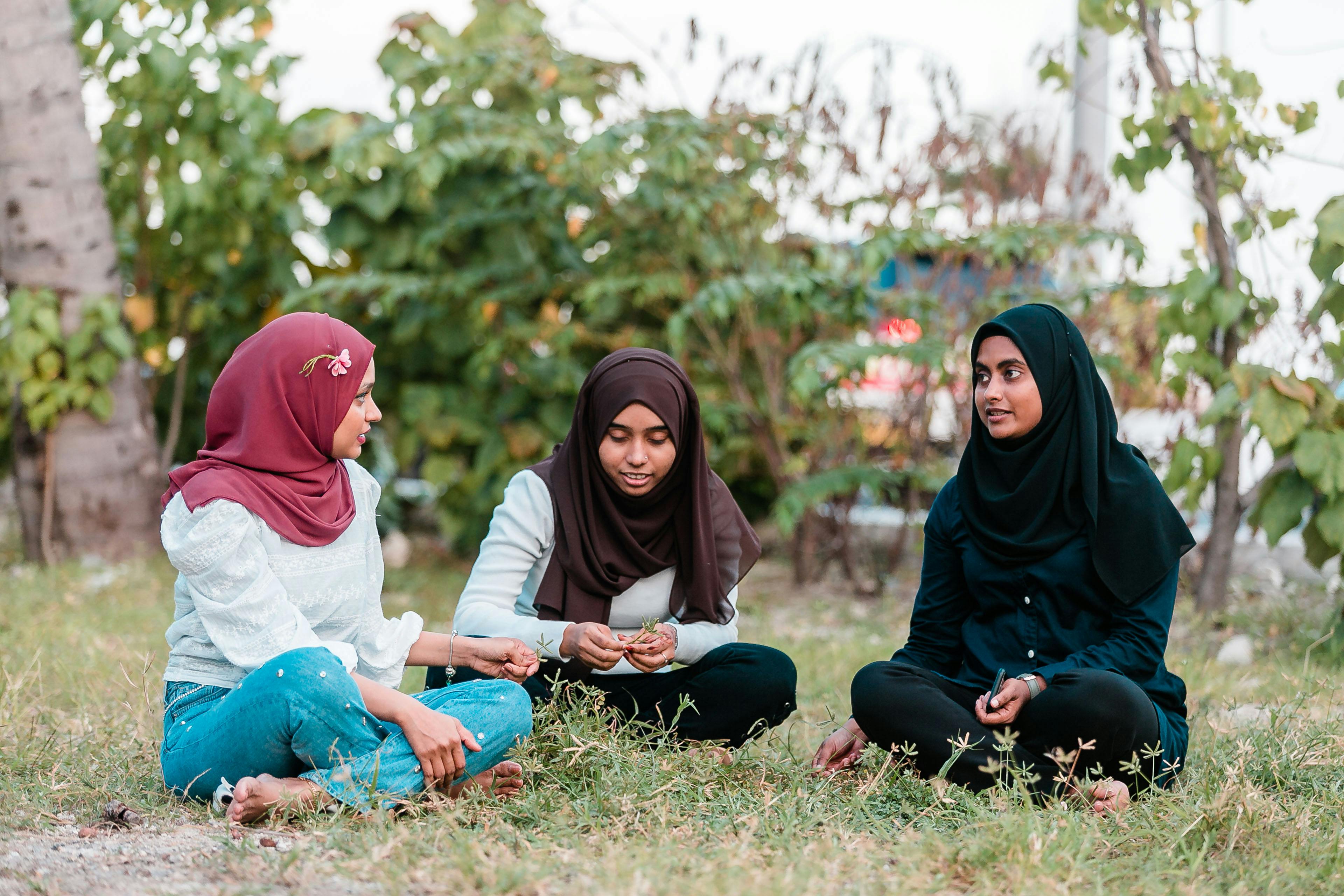 muslim women sitting on grass in park and talking