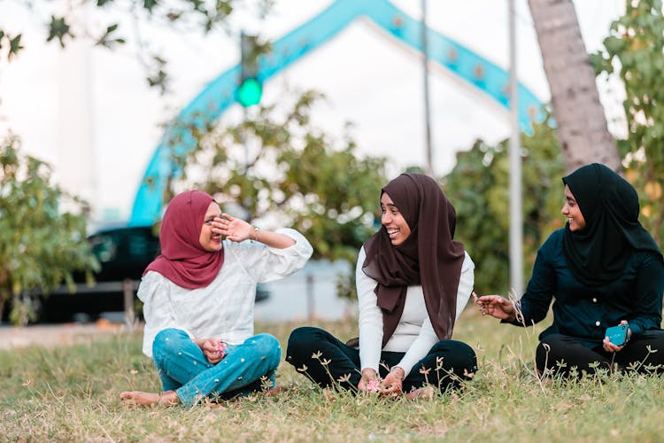 Young Muslim Women Laughing While Resting On Grass