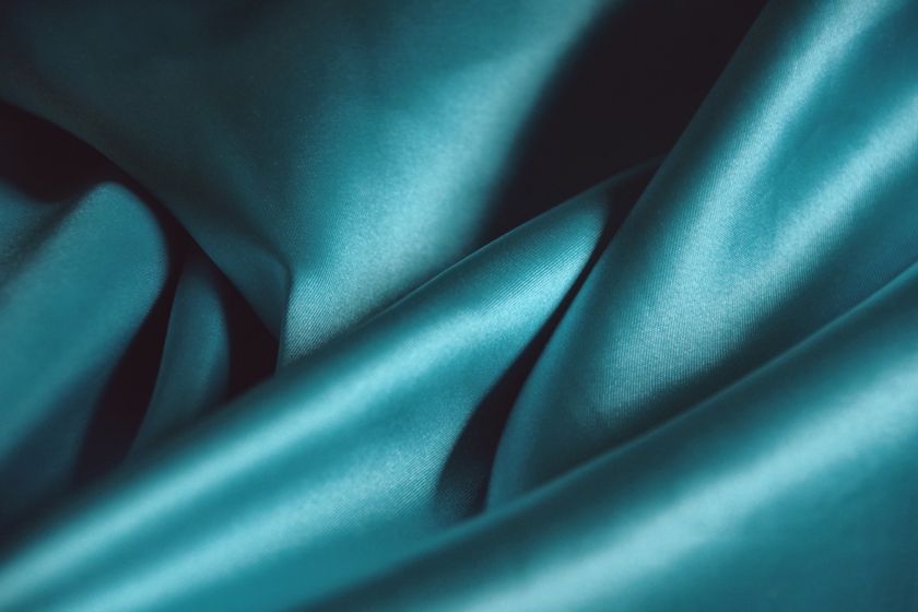 Close-up of a teal silk cloth in fluid folds, the lustre travelling along the crest of each fold.