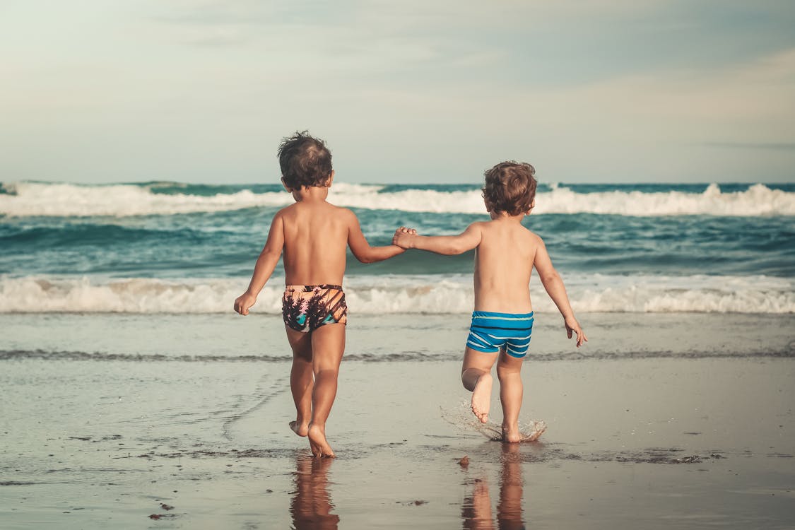 Meninos Irreconhecíveis De Mãos Dadas E Caminhando Na Praia Arenosa