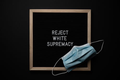 Top view of disposable mask on chalkboard with Reject White Supremacy inscription on black background