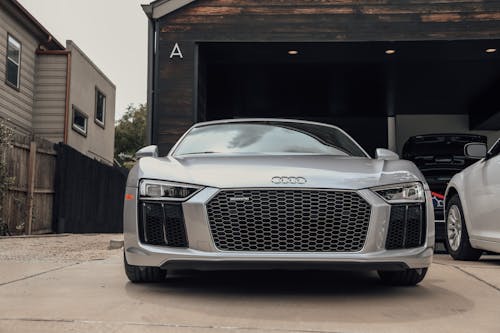 Front part of expensive gray luxury sports car with big grille and glossy surface parked on pavement by simple construction in daylight