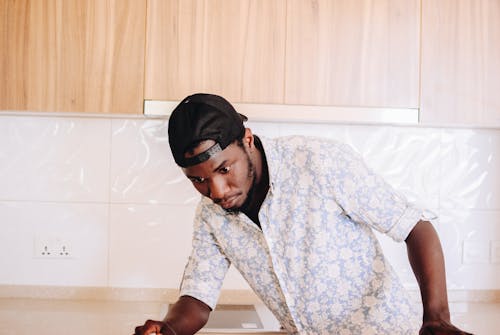 Free Concentrated African American male in shirt and black cap cleaning surface of table in bright cozy apartment decorated in pastel colors Stock Photo