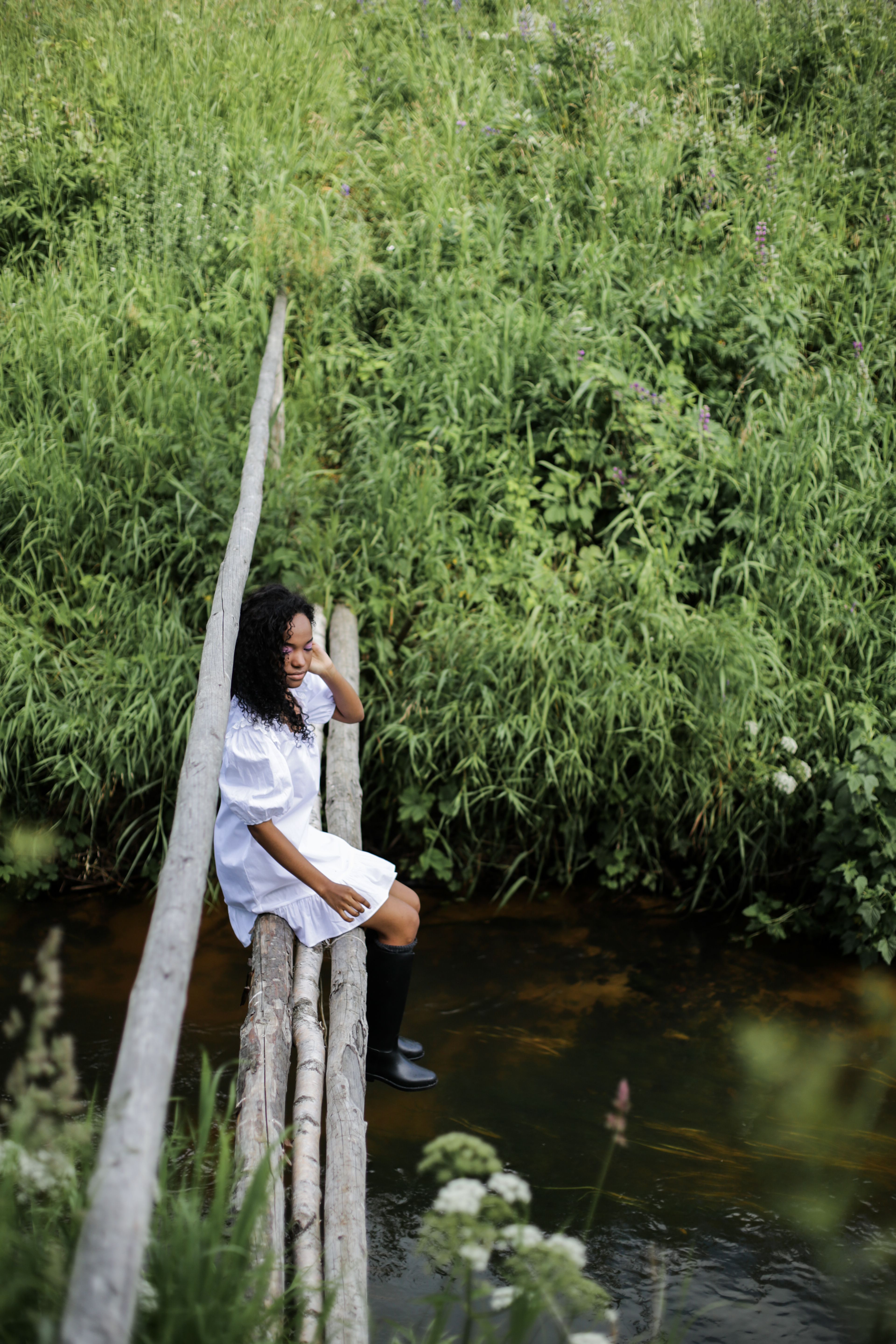 一名身穿白色连衣裙的女子坐在一座环绕着绿色植物的乡村桥上