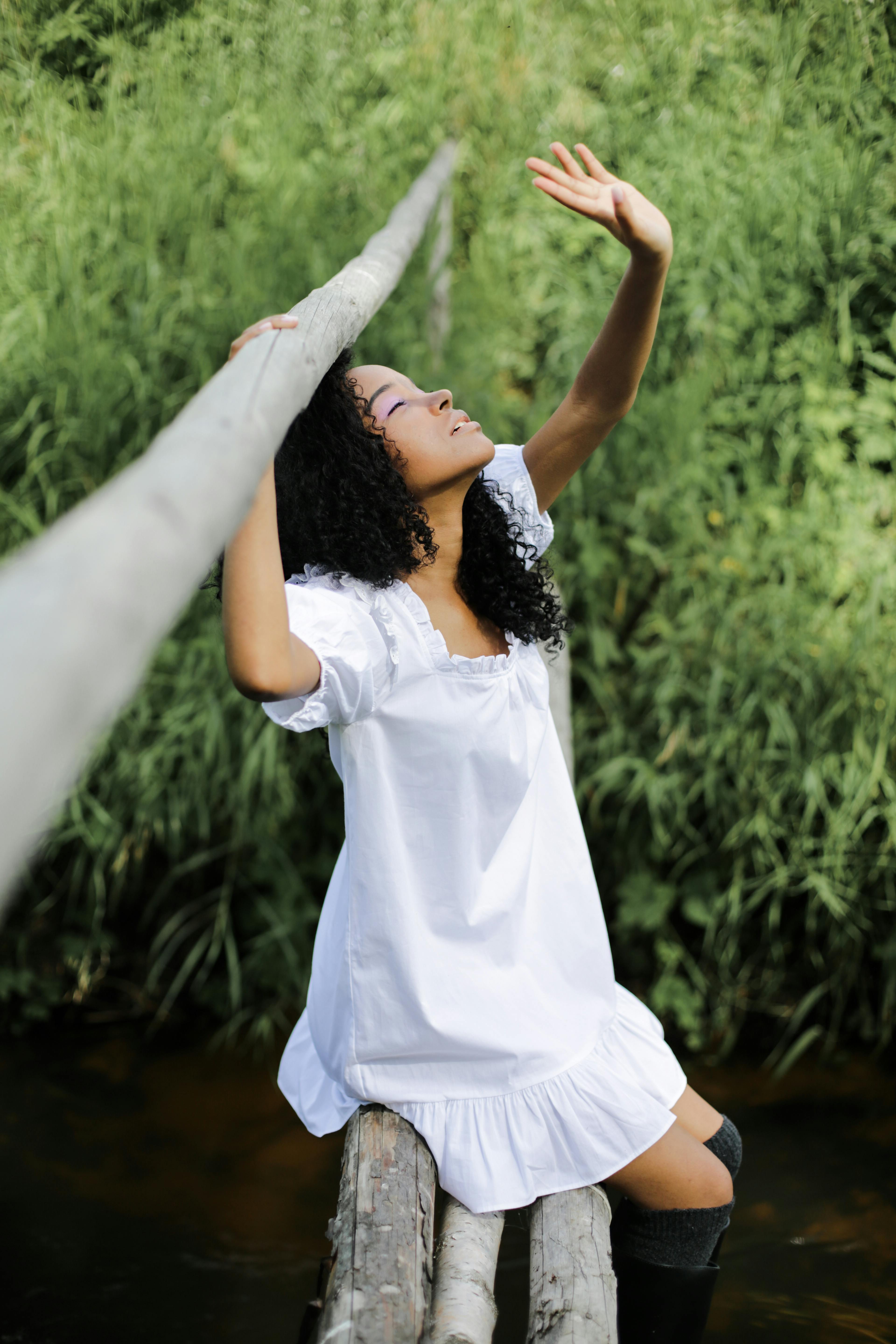 一位年轻女子身穿白色连衣裙，坐在一座绿树环绕的乡村桥上