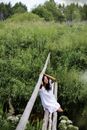 一位身穿白裙的女子坐在乡村桥上，四周郁郁葱葱的绿植环绕，构成一幅宁静的景象