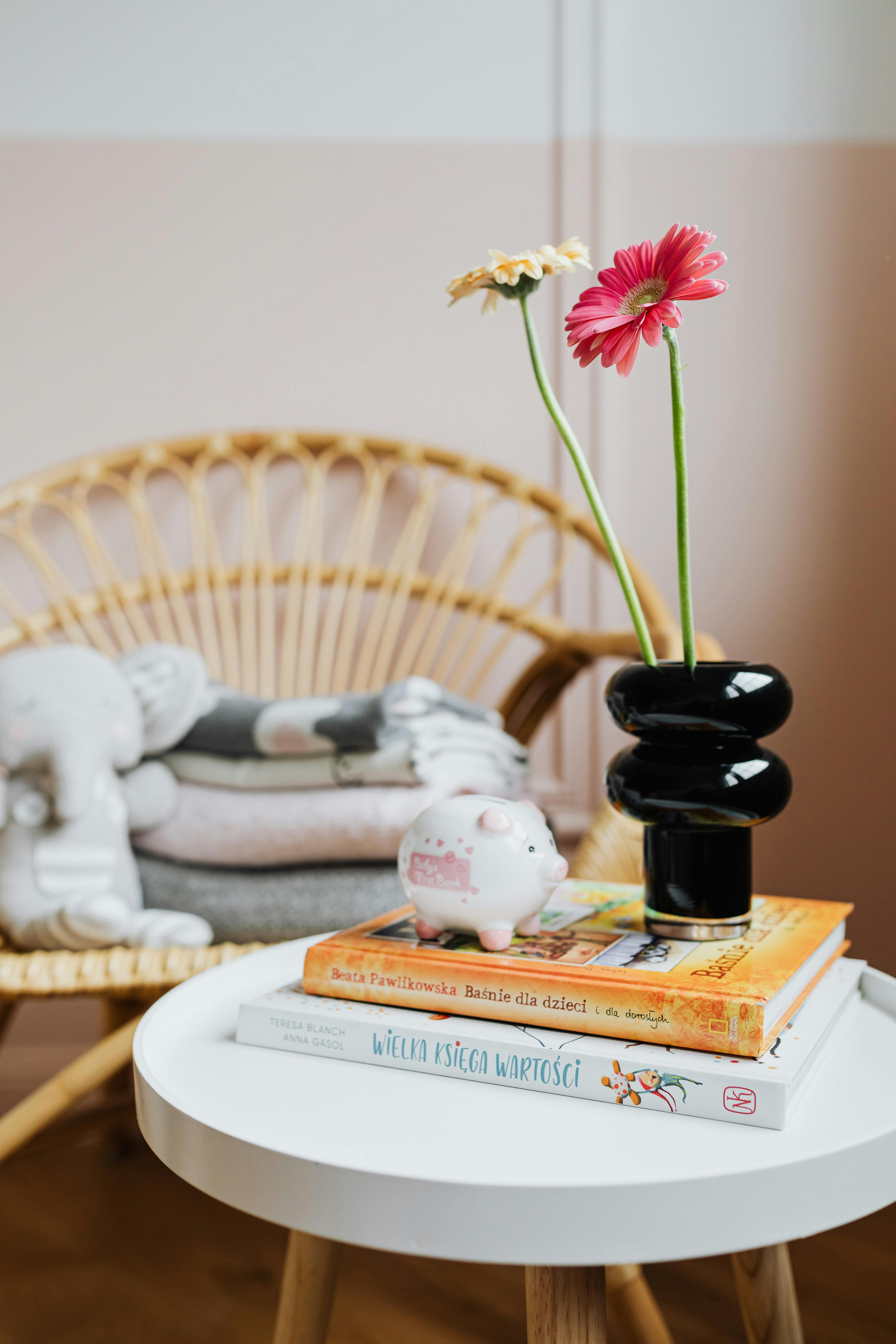 Free Modern nursery with gerbera flowers in a vase on a table alongside children's books and a piggy bank. Stock Photo