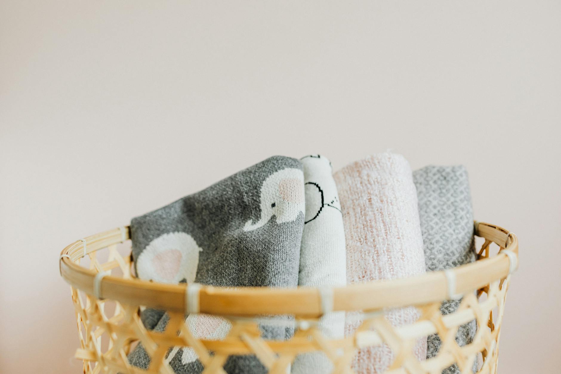 Soft patterned blankets arranged in a wicker basket against a neutral background.