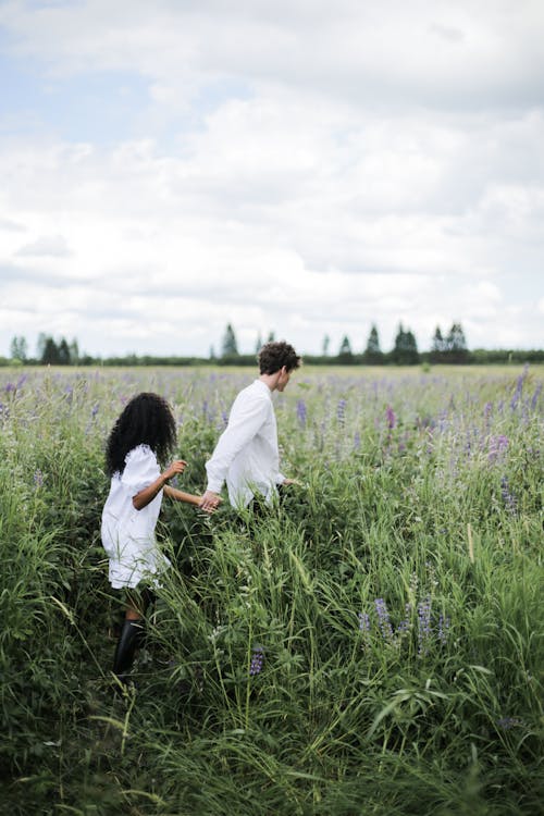 Man and Woman Holding Hands While Walking on Green Grass Field