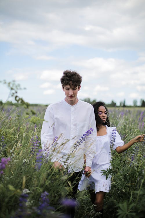 Man in White Dress Shirt Standing Beside Woman in White Dress on Purple Flower Field during