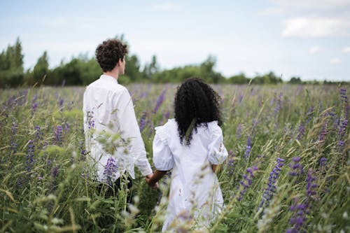Man and Woman in White Dress Walking on Green Grass Field