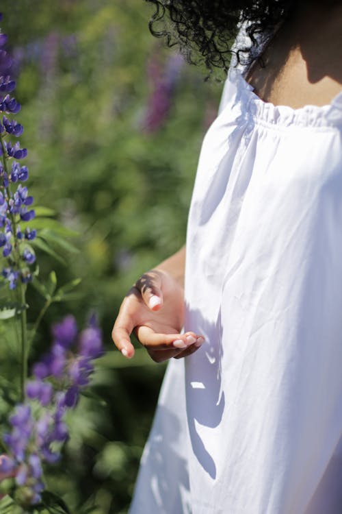 Woman in White Dress Standing Near Purple Flowers