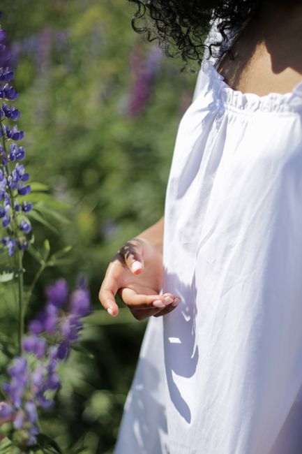 A close-up of a person in a white dress gently touching purple lupine flowers in a field.